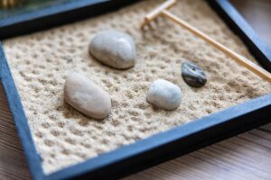 Giardino zen in un vassoio con sabbia, sassi e rastrello, simbolo di tranquillità e meditazione.